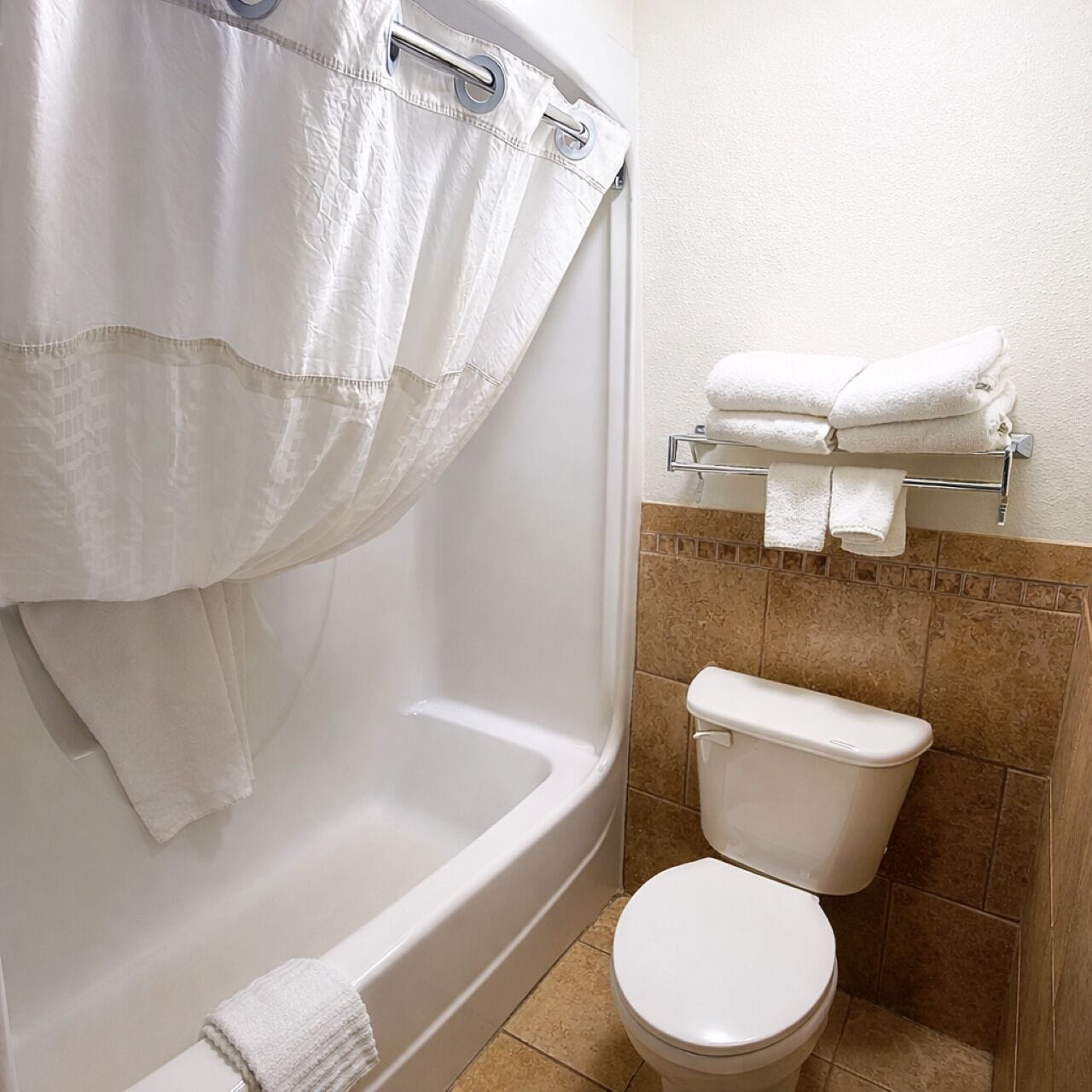 A bathroom with a bathtub, toilet, and a towel rack with folded towels.