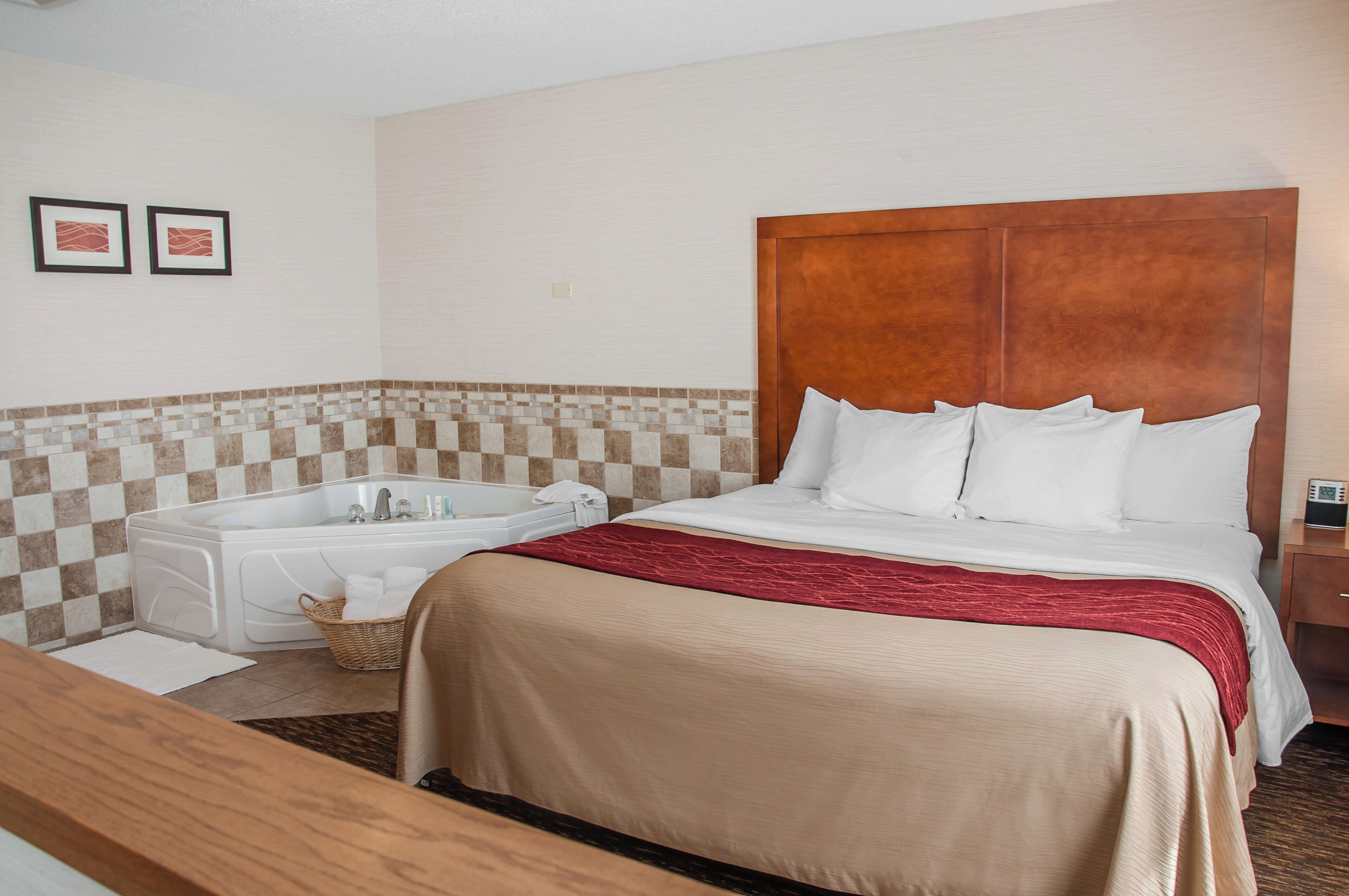 A hotel room with a large bed, a wooden headboard, a white bathtub, and a checkered tile backsplash.