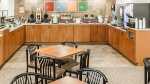 Un espace cuisine moderne avec une table et des chaises en bois, équipé de différents types de machines à café et d’un réfrigérateur.