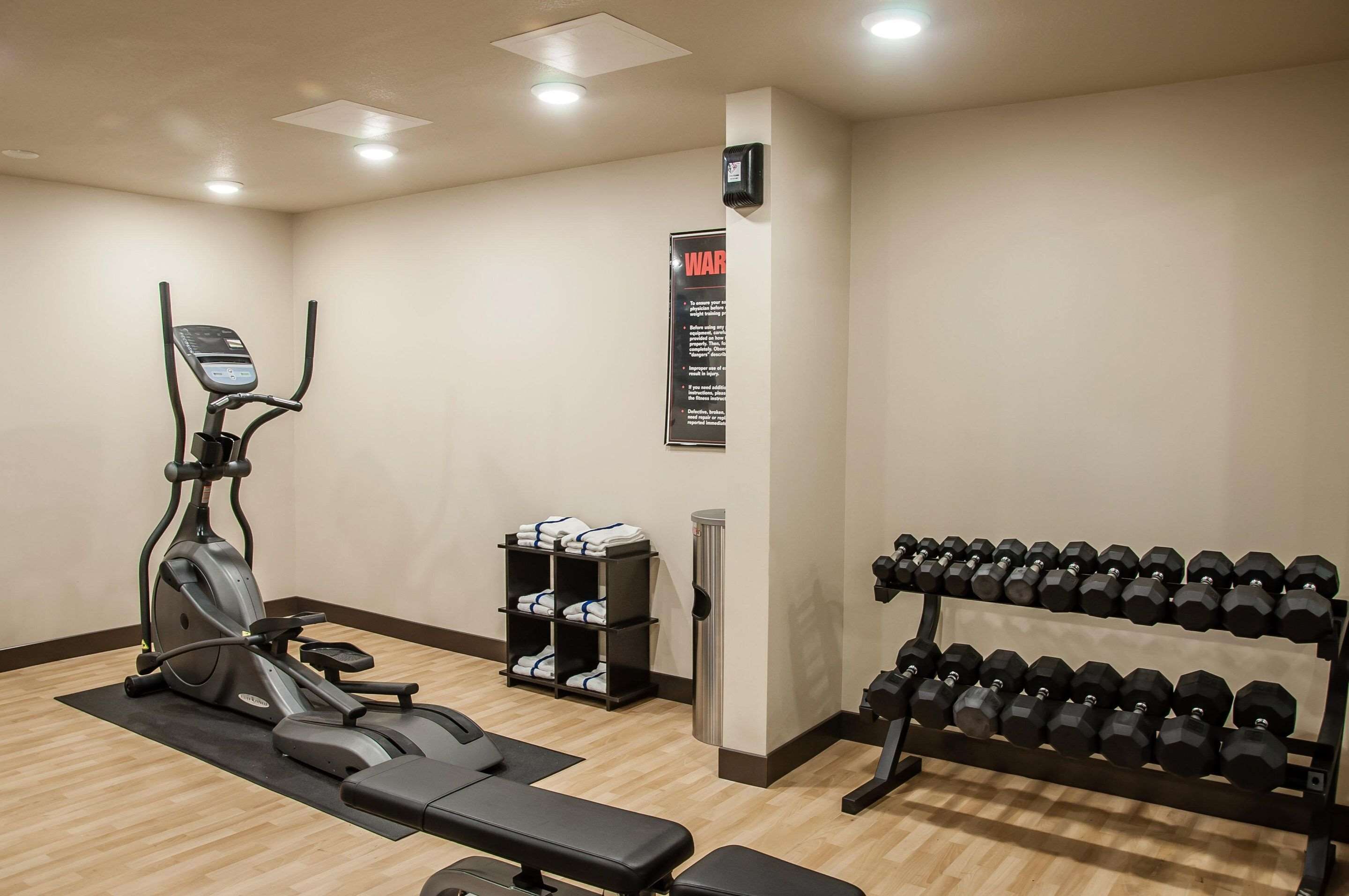 A gym with an elliptical machine, a bench, a rack of dumbbells, and a shelf with towels.