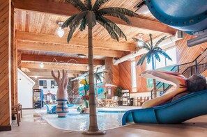 Un área de piscina interior con un tobogán, una palmera y una gran fuente de agua azul.