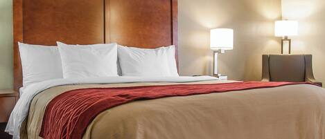 A hotel room with a large bed, a wooden headboard, two bedside lamps, and a red throw blanket.