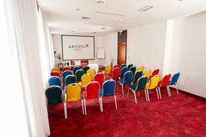 A conference room with rows of colorful chairs, a whiteboard, and a projector screen displaying "ARCOTEL HOTELS".