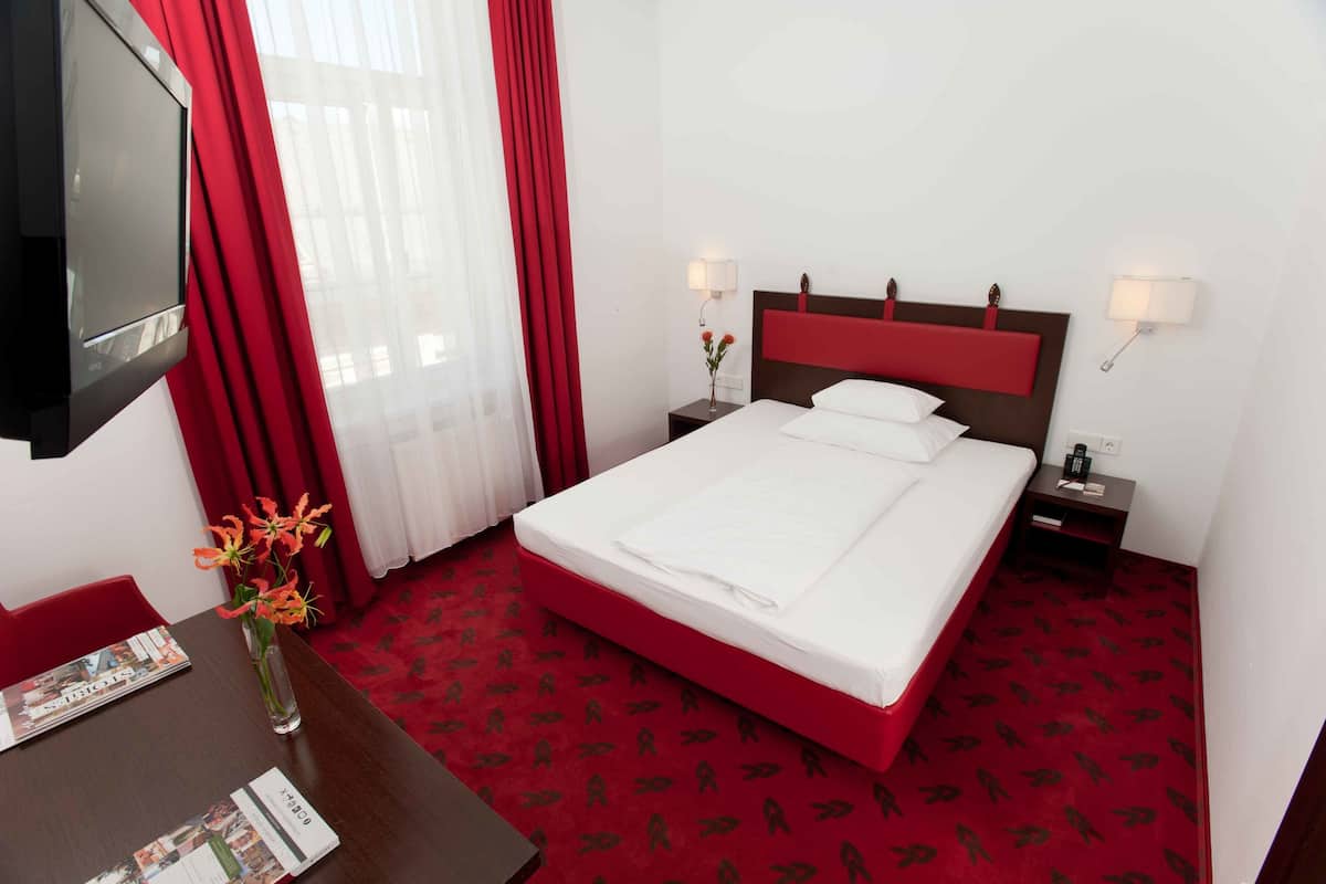 Una habitación de hotel con una cama grande, cortinas rojas, un televisor y un escritorio con un florero.