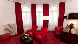 A hotel room with a red carpet, red furniture, a TV, and a radiator. - Garner Hotel Klagenfurt - Moser Verdino (Klagenfurt am Woerthersee)