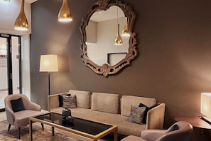 A modern living room with a beige sofa, two armchairs, a glass coffee table, and a large ornate mirror.