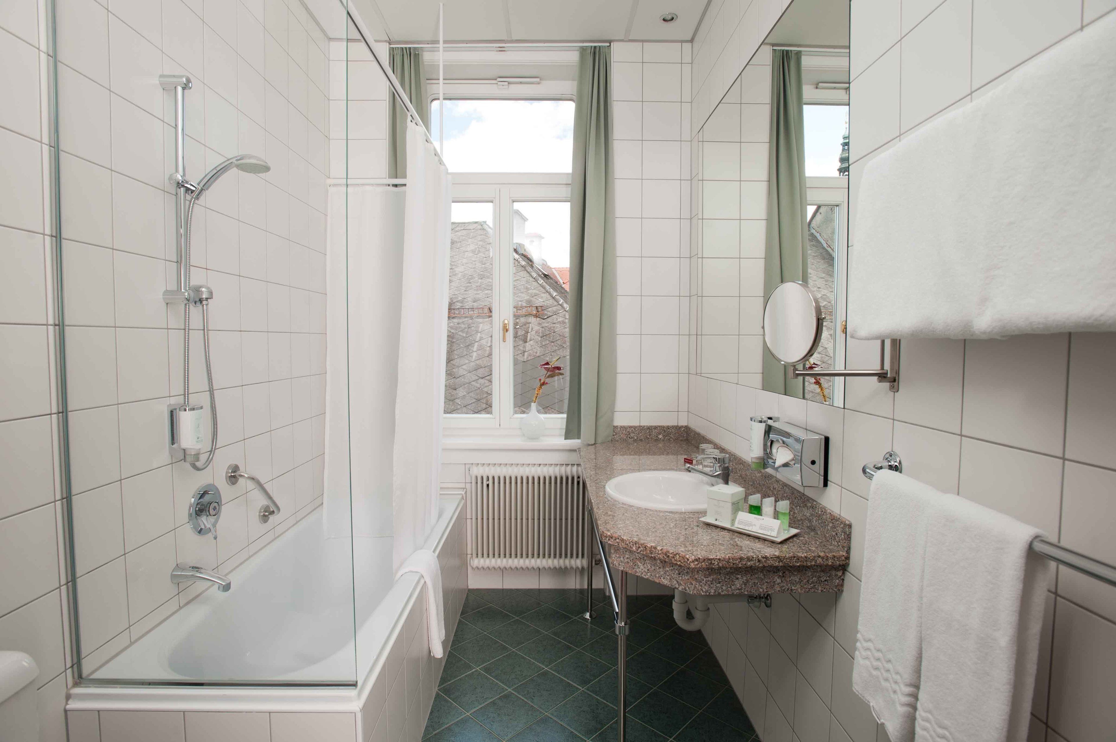 Un baño moderno con ducha de vidrio, un lavabo con encimera de granito, un espejo y un perchero para toallas.