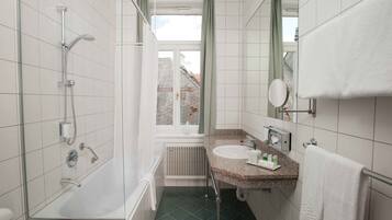 Un baño moderno con ducha de vidrio, un lavabo con encimera de granito, un espejo y un perchero para toallas.