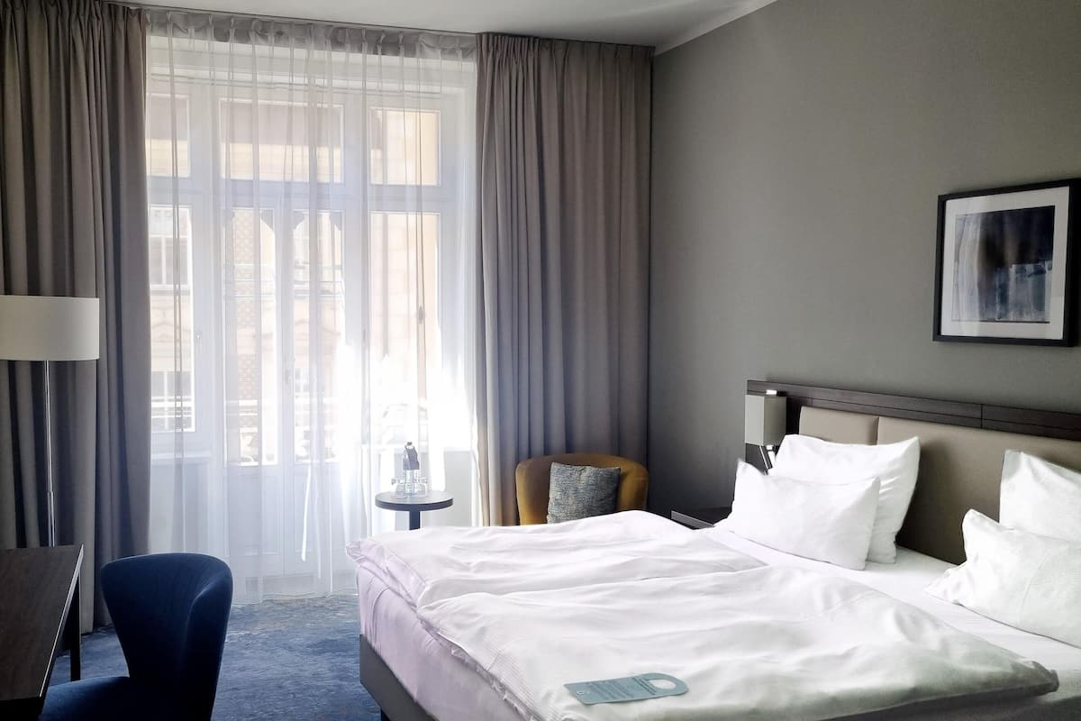 Habitación de hotel con cama, una silla, una mesita y ventana con cortinas.
