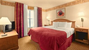 A hotel room with a large bed, a television on a wooden nightstand, and a window with curtains. - Pan American Inn & Suites (Albuquerque)