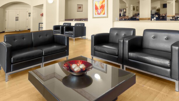 A modern lounge area with black leather sofas, a glass coffee table, and a view of the kitchen in the background. - Pan American Inn & Suites (Albuquerque)