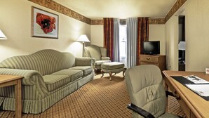A hotel room with a striped sofa, a chair, a small table, a desk, a television, and a window with curtains. - Pan American Inn & Suites (Albuquerque)