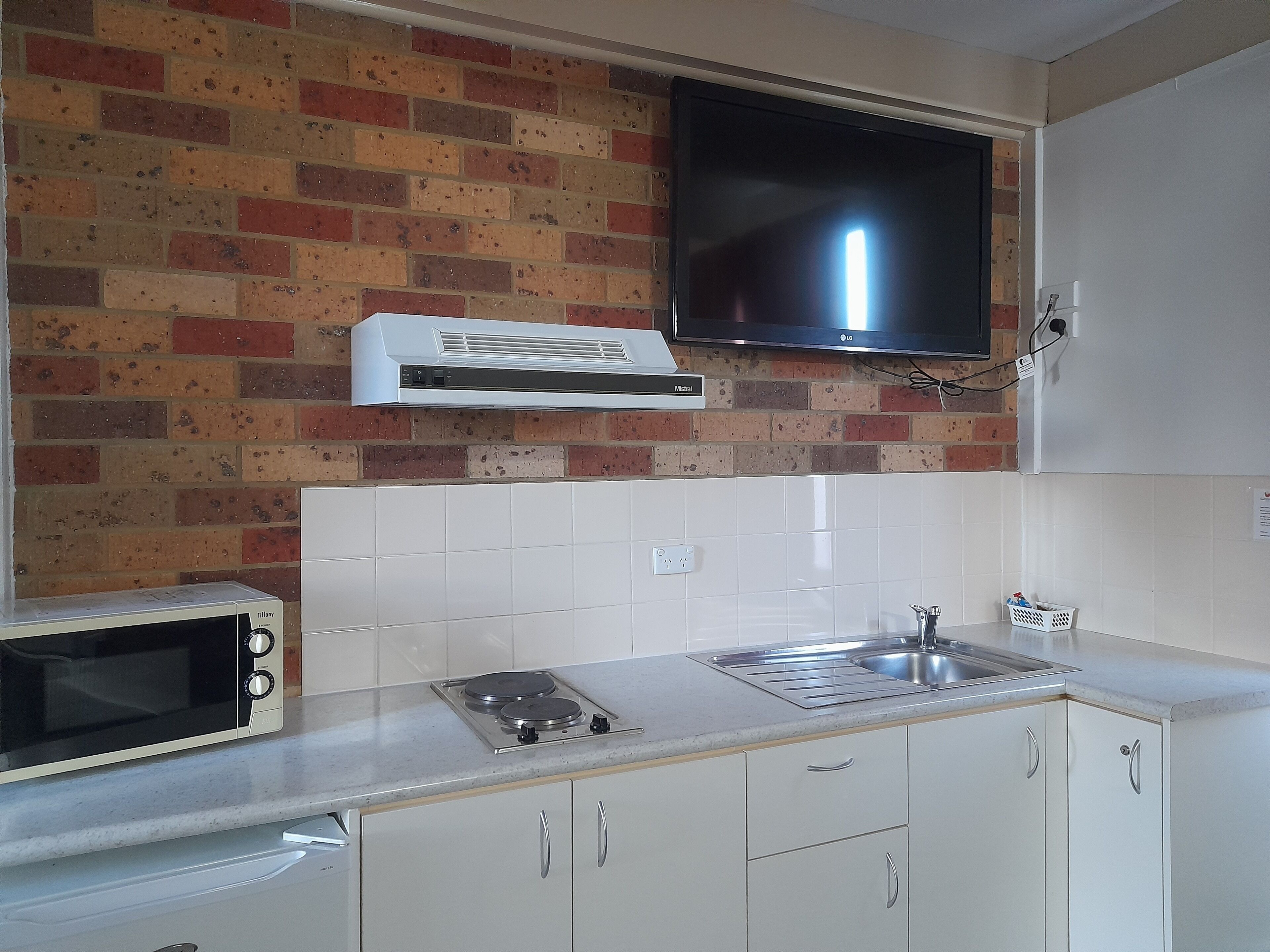 A kitchen with a brick wall, a flat-screen TV, a microwave, a stove, and a sink.