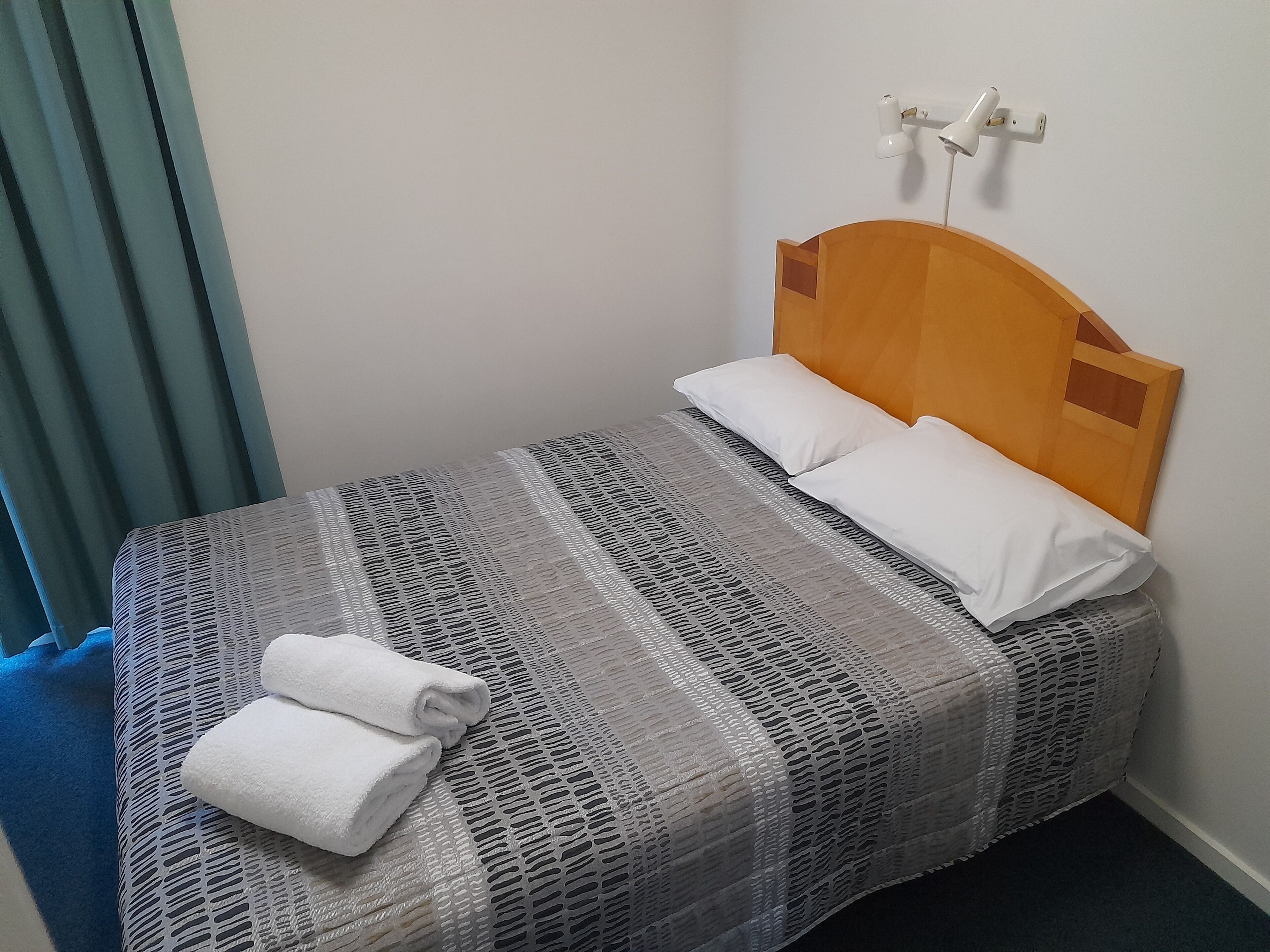 Ein ordentlich bezogenes Bett mit gestreifter Tagesdecke, zwei Kissen und einem gefalteten Handtuch auf der Seite.