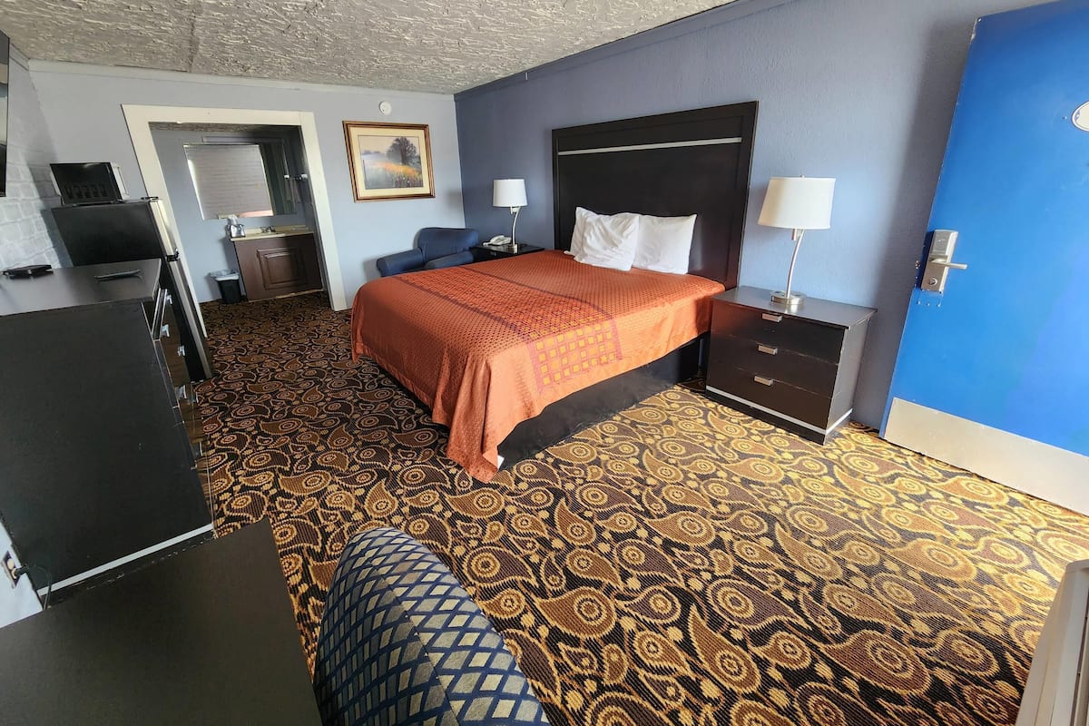 Hotelkamer met een bed, bureau, stoel, televisie, schilderij en een kamerbreed tapijt.