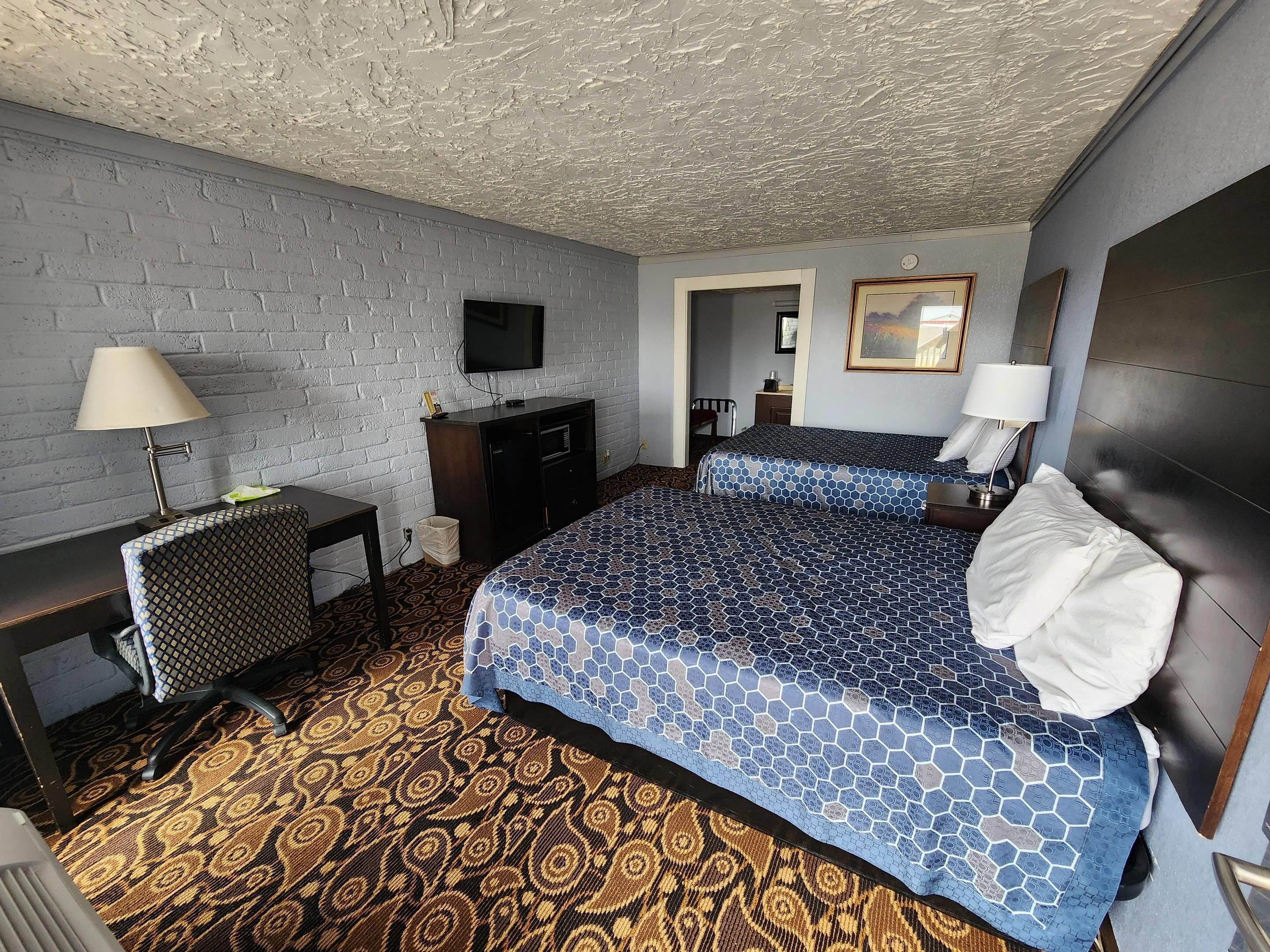 A hotel room with two beds, a TV, a desk with a lamp, and a patterned carpet.