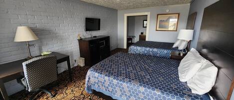 A hotel room with two beds, a TV, a desk with a lamp, and a patterned carpet.