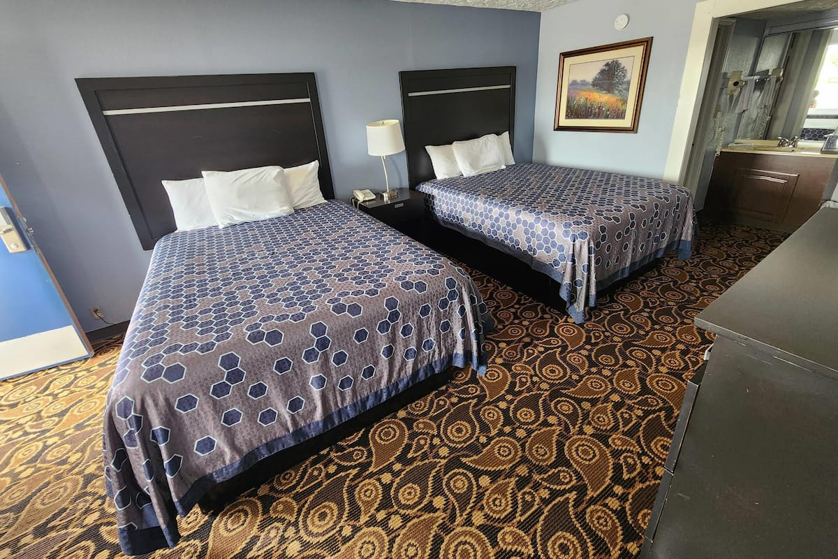 Een hotelkamer met twee bedden, een kamerbreed tapijt met dessin, een schilderij aan de muur en een klein bureau.