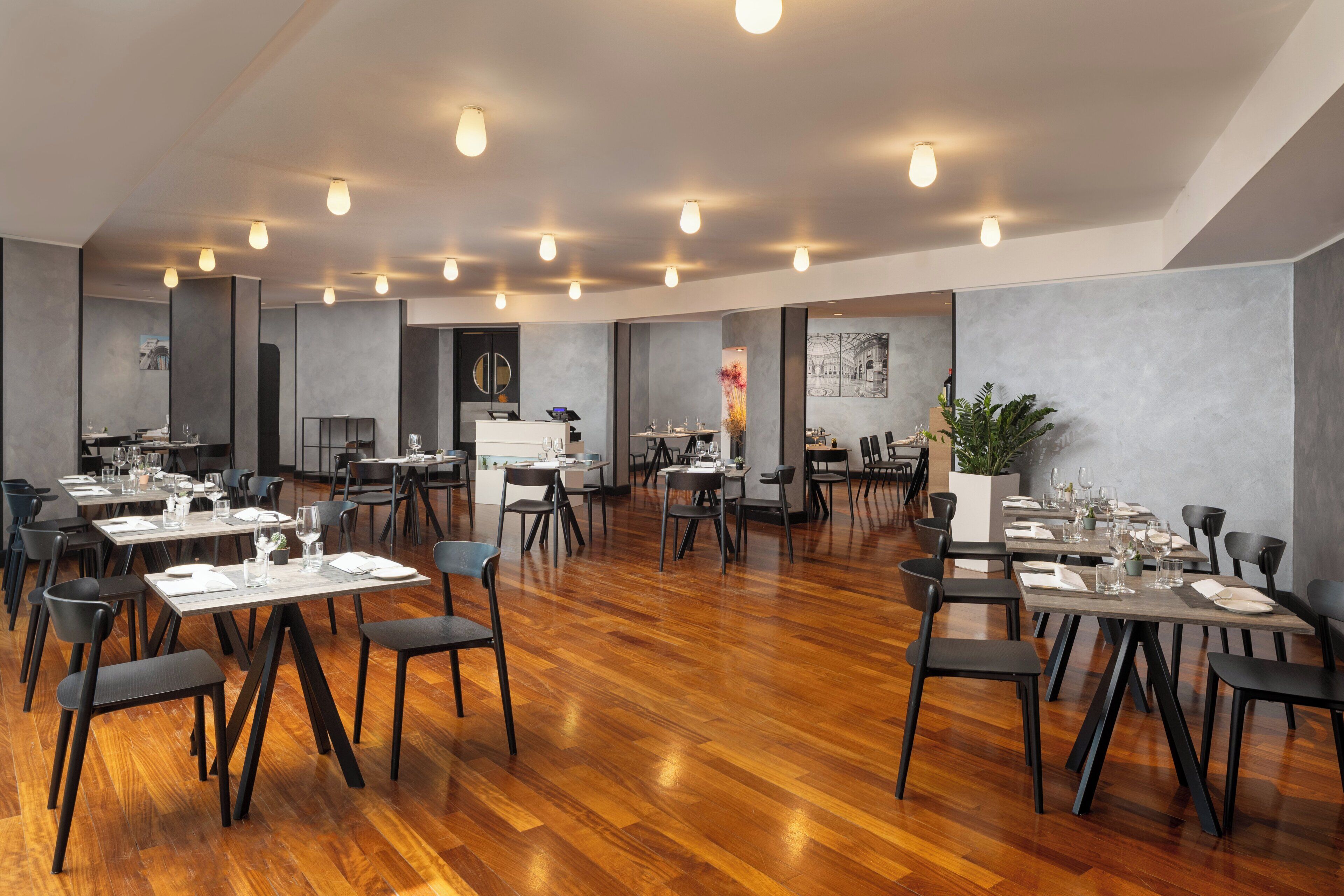 A spacious dining area with multiple tables and chairs, wooden flooring, and modern lighting fixtures.