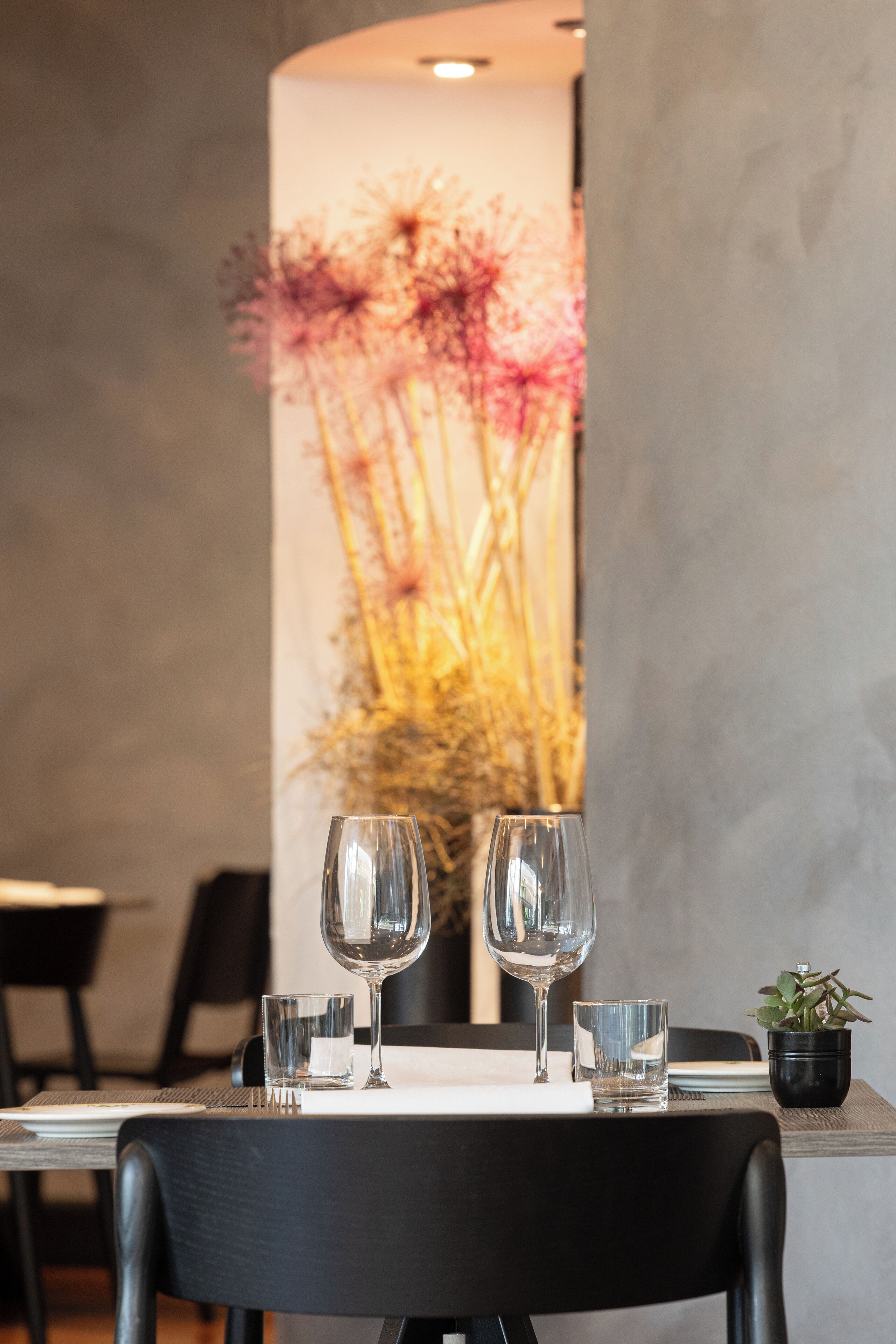 A dining table with two wine glasses and a small plant, set against a wall with a floral mural.