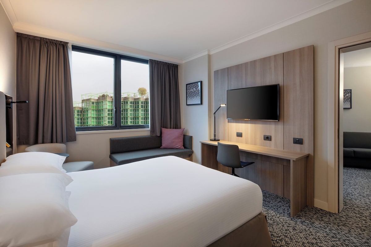 A hotel room with a bed, desk, chair, TV, and large window.