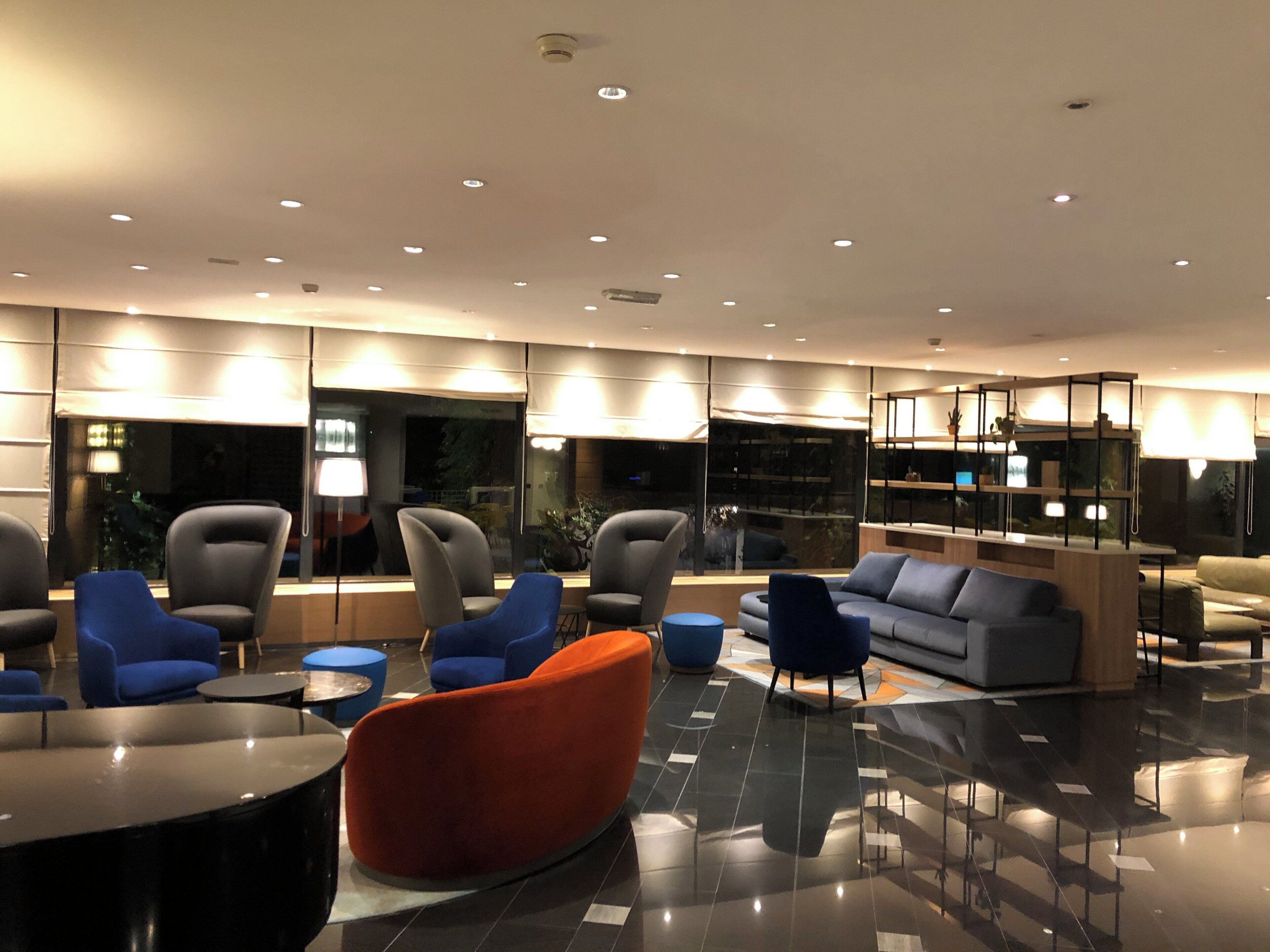 Un hall d’entrée moderne, doté d’espaces de détente, d’un comptoir d’accueil et d’une grande fenêtre offrant une vue sur l’extérieur.