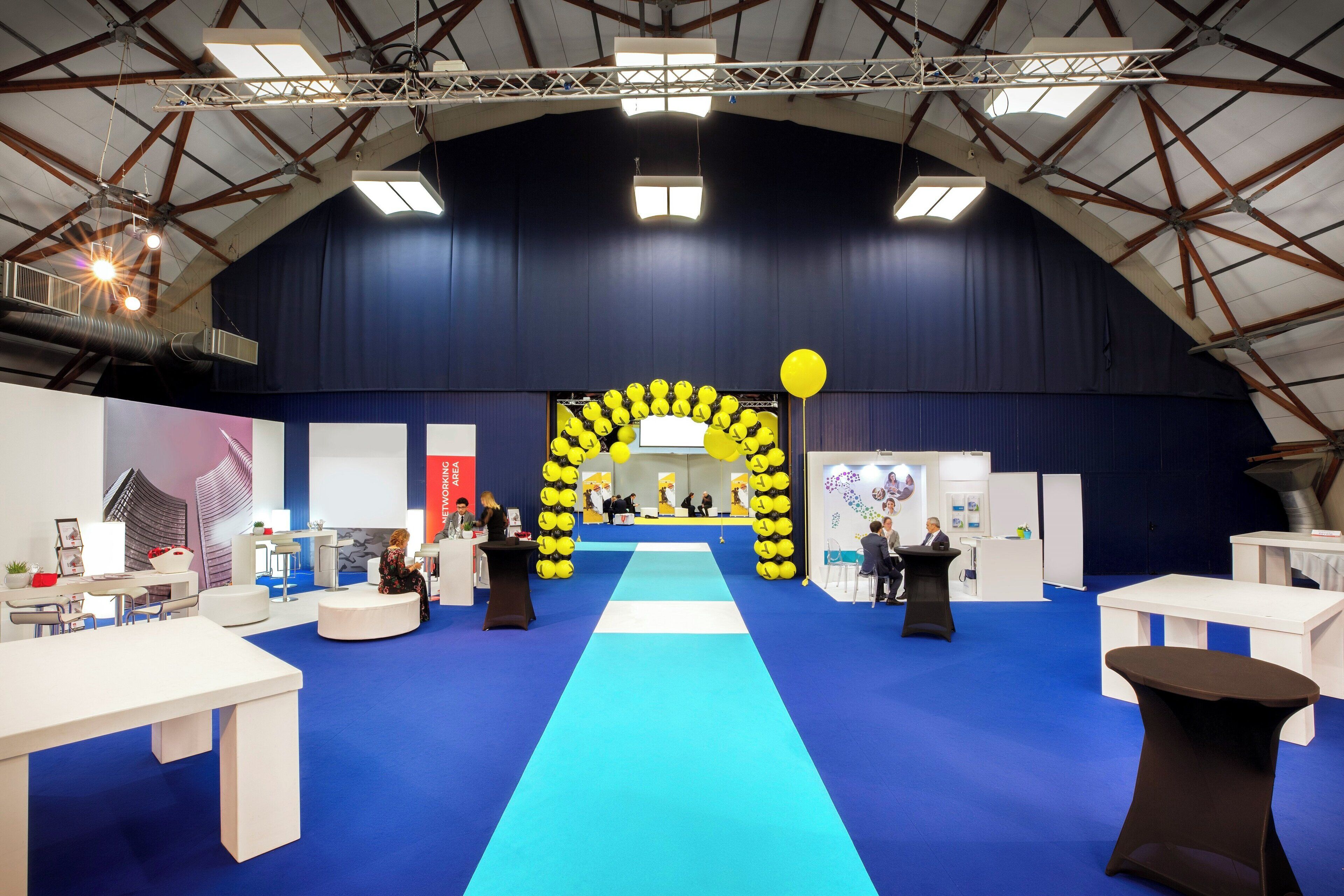 An indoor exhibition space with a central stage, booths, and a blue carpet.