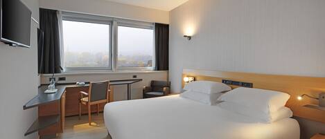 Una habitación de hotel moderna con una cama grande, un escritorio, una silla y un televisor en la pared.