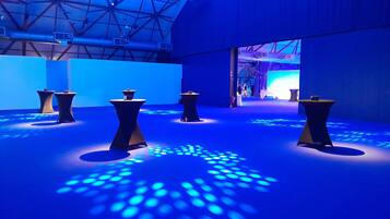 Un interior moderno con patrones de iluminación geométricos, un techo alto y un pasillo central que conduce a una zona de escenario.