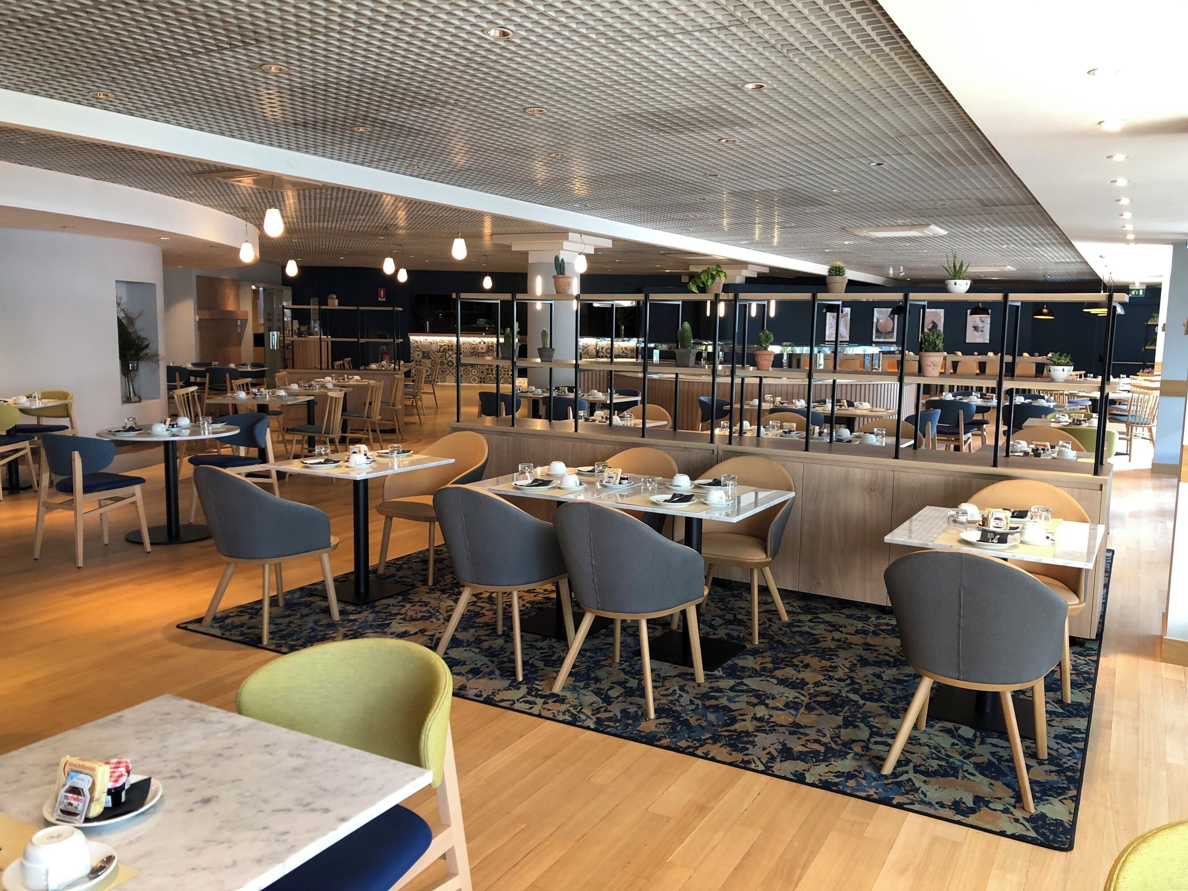 A modern restaurant with multiple dining areas, wooden flooring, and a patterned ceiling.