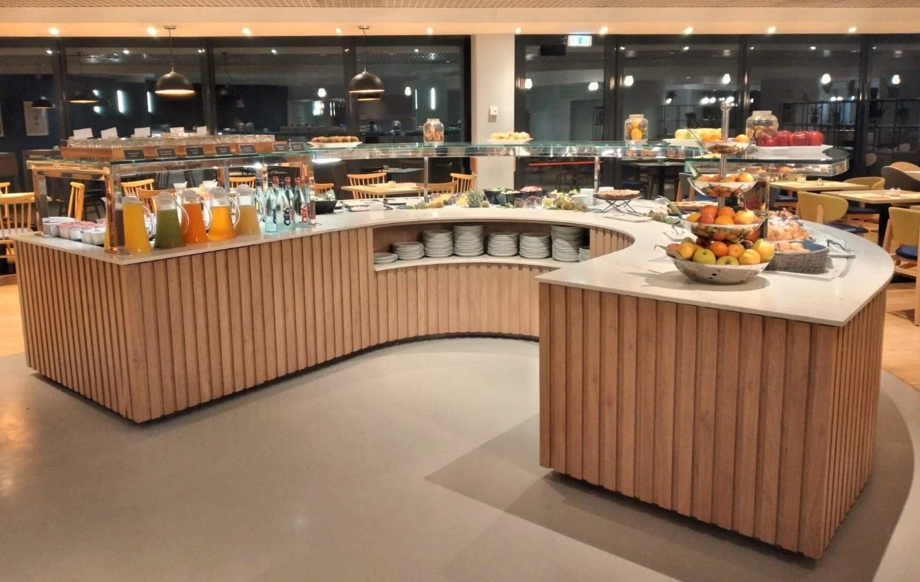 A buffet area with a curved counter, various food and drink options, and seating arrangements.