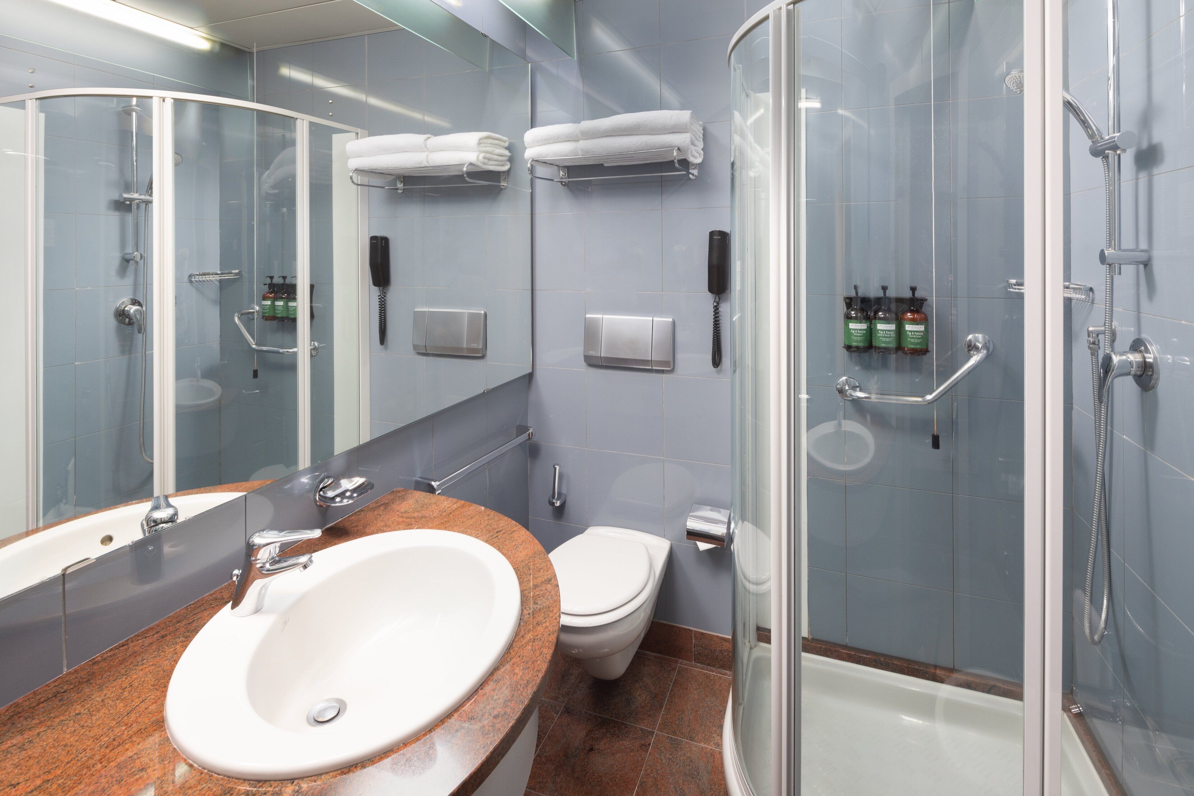 Un baño moderno con cabina de ducha de vidrio, un lavabo blanco con encimera de granito, inodoro y un espejo grande.