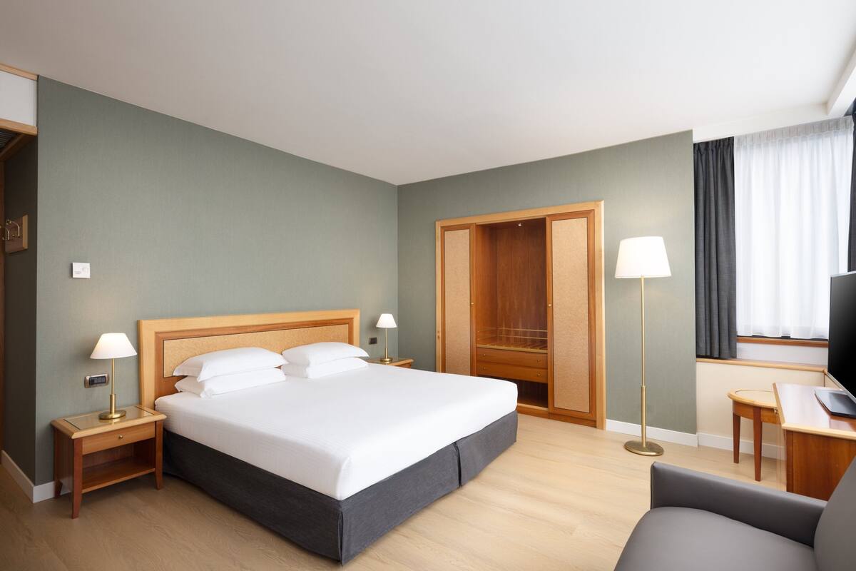 A hotel room with a bed, bedside tables, a desk, and a TV.