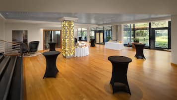 A spacious lobby with a wooden floor, black round tables, and a central decorative pillar.
