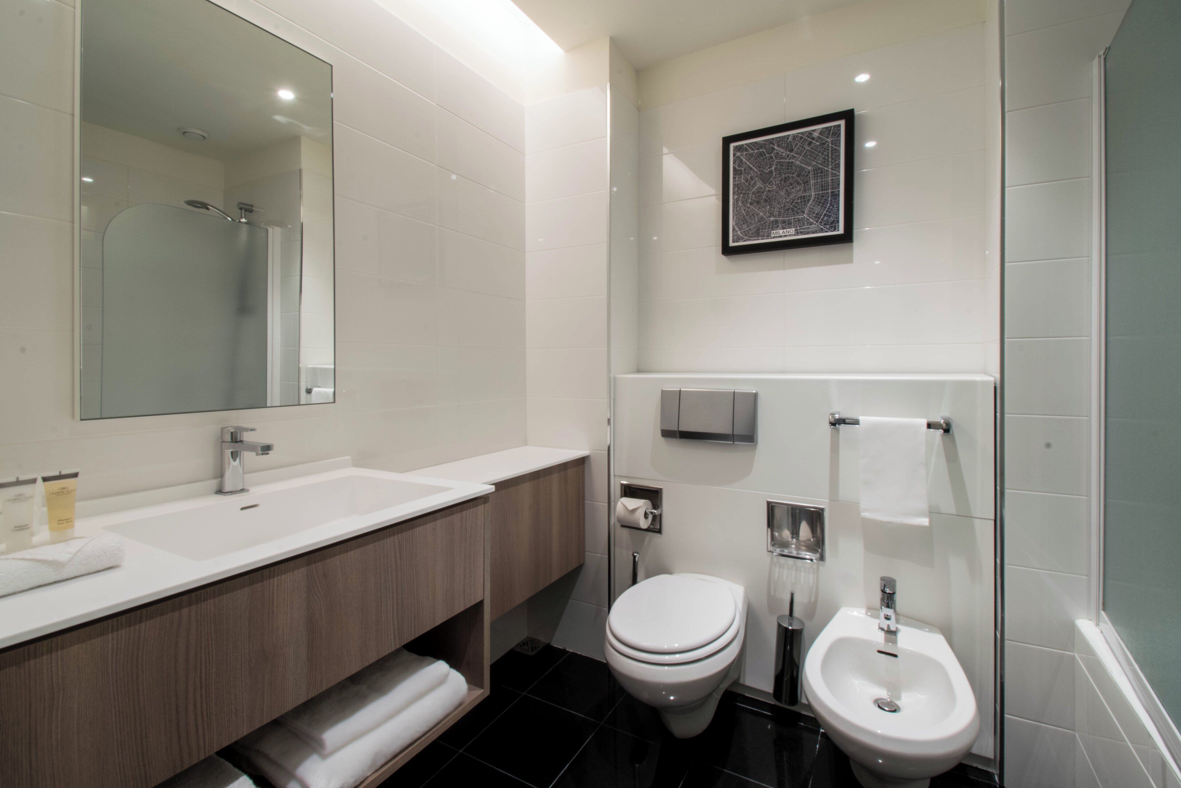 Een moderne badkamer met een grote spiegel, een wastafel, toilet en een bidet.