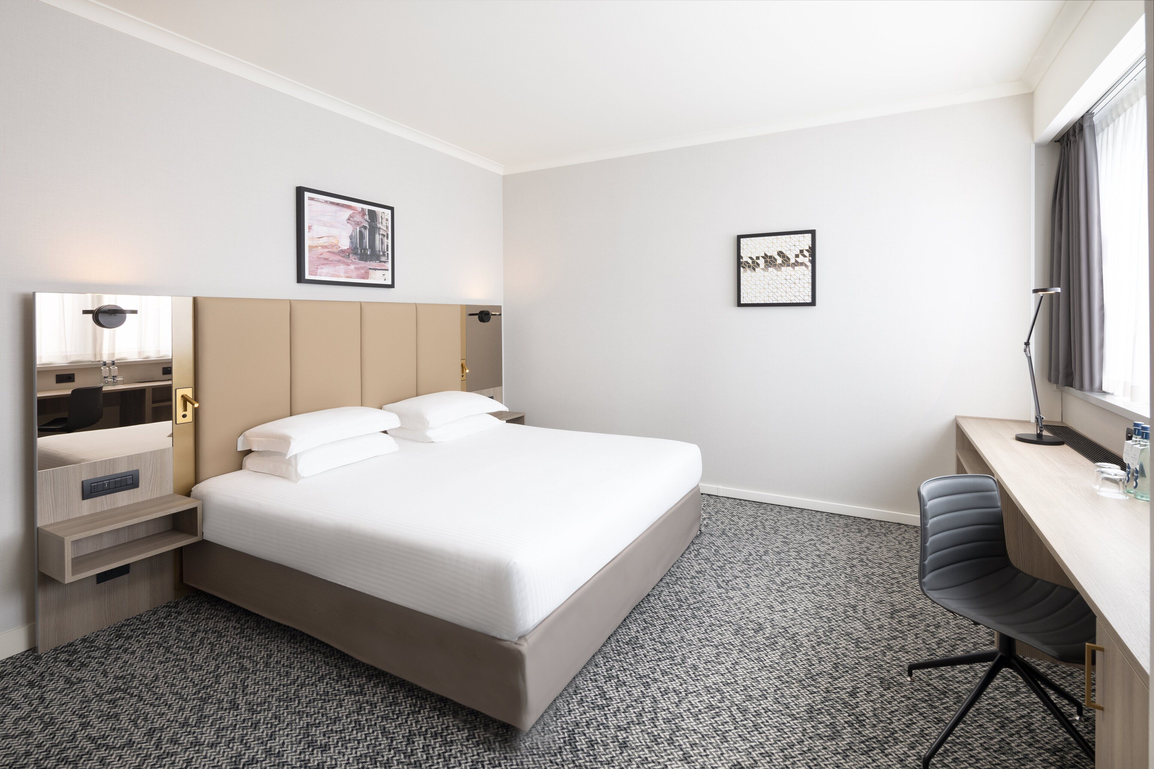 Une chambre d’hôtel avec un lit, un bureau, une chaise, une armoire et deux tableaux encadrés au mur.