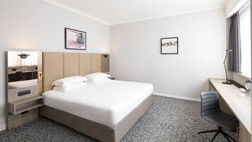 Une chambre d’hôtel avec un lit, un bureau, une chaise, une armoire et deux tableaux encadrés au mur.