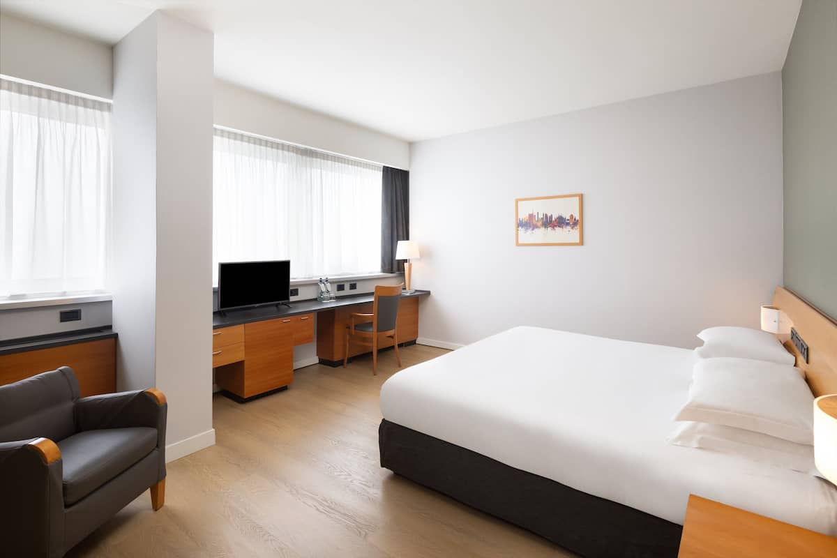A hotel room with a bed, a desk, a chair, a TV, and a window with curtains.