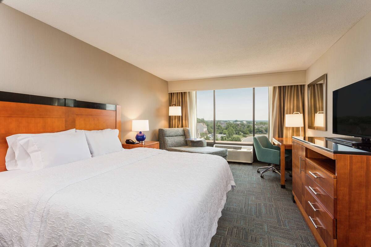 A hotel room with a large bed, a desk with a television, a chair, and a view of the city.