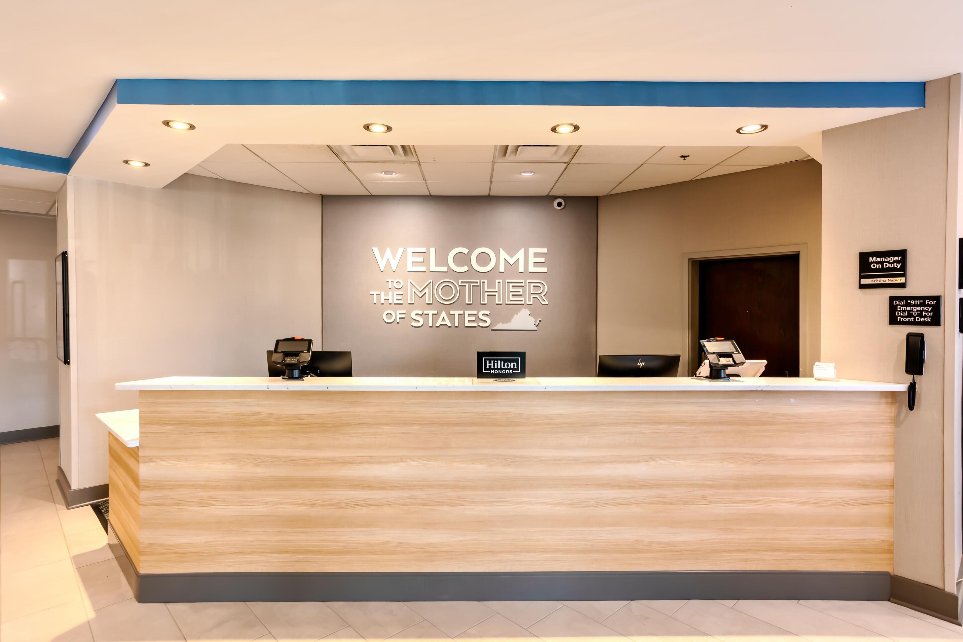 Un mostrador de recepción de hotel con un letrero que dice 'Welcome to the Mother of States', una pantalla digital y un letrero que indica 'Gerente de guardia'.