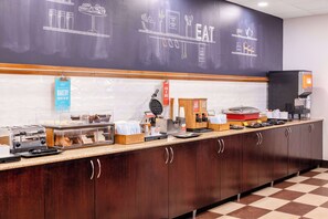 A buffet counter with various food items, a coffee machine, and a chalkboard with food-related drawings. - Hampton Inn Manassas (Manassas)