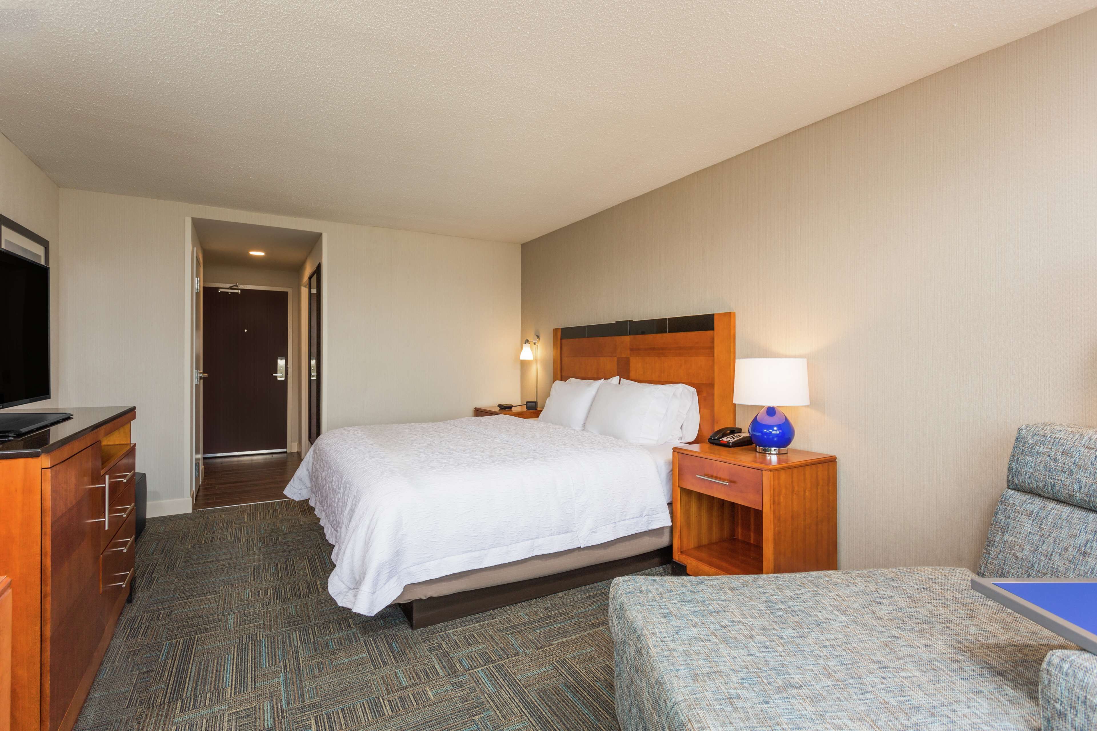 A hotel room with a bed, a desk, a chair, and a television.