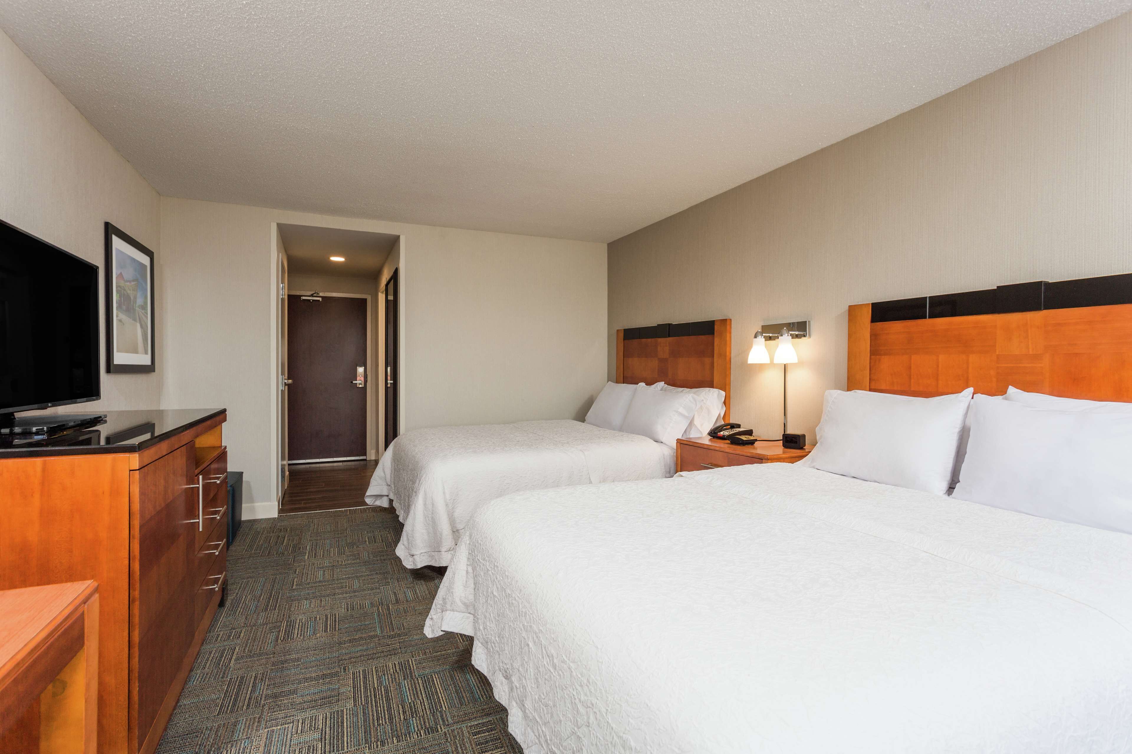A hotel room with two beds, a TV, a desk, and a lamp.