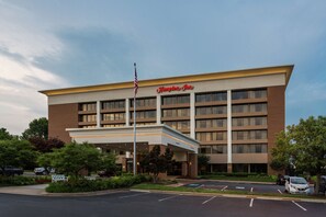 A hotel with a prominent entrance, a flag, and a parking lot. - Hampton Inn Manassas (Manassas)