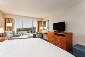 A hotel room with a large bed, a desk, a television, and a view of the cityscape.