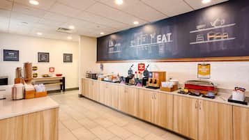 Un bar où l’on peut prendre le petit-déjeuner, avec un tableau noir servant de menu, une machine à café et divers produits pour le petit-déjeuner.