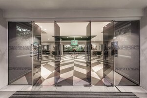 Un moderno vestíbulo de hotel con un suelo de diseño geométrico, puertas de cristal y un área de descanso central.