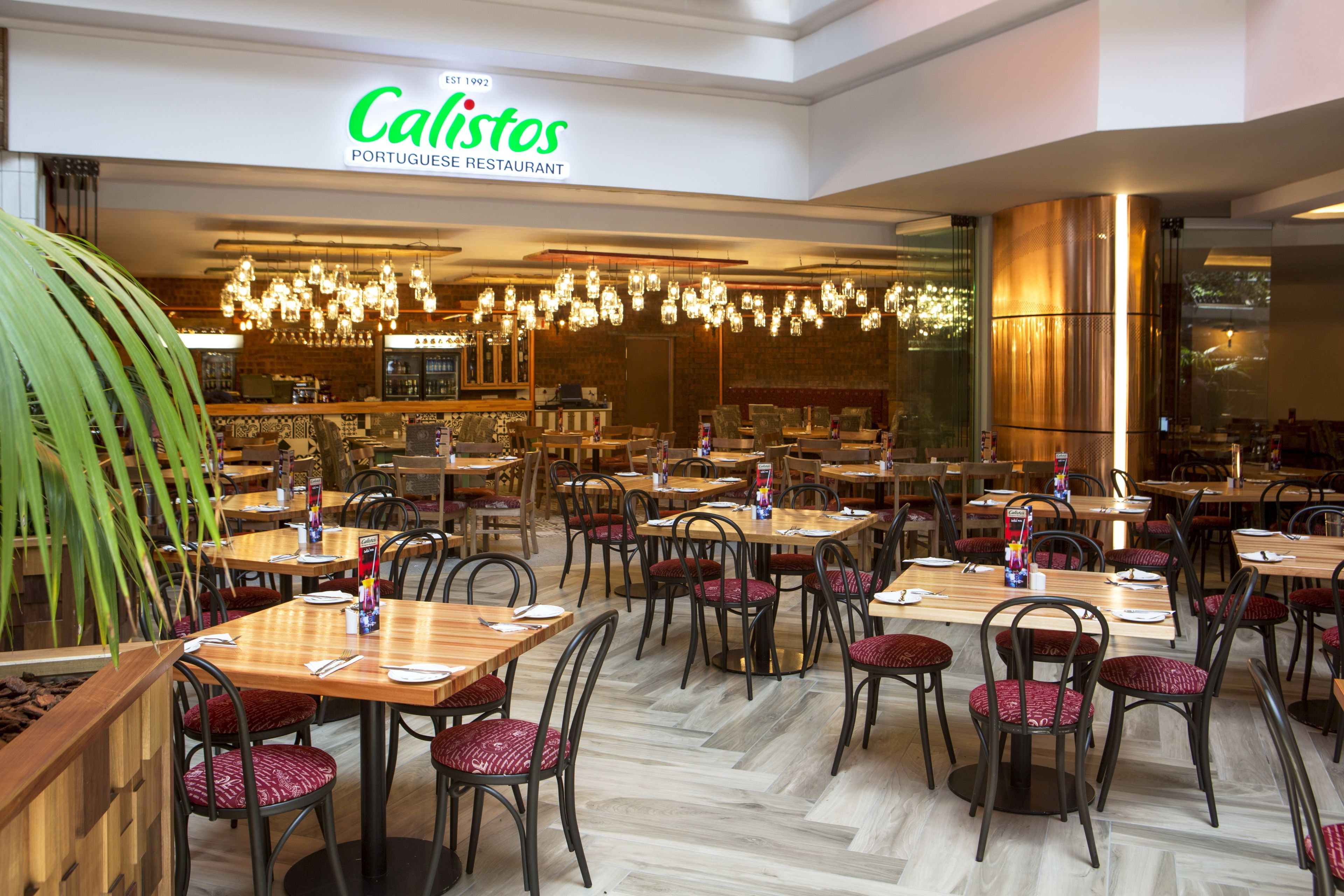 A restaurant interior with multiple tables and chairs, a visible menu board, and a sign indicating it's a Portuguese restaurant.