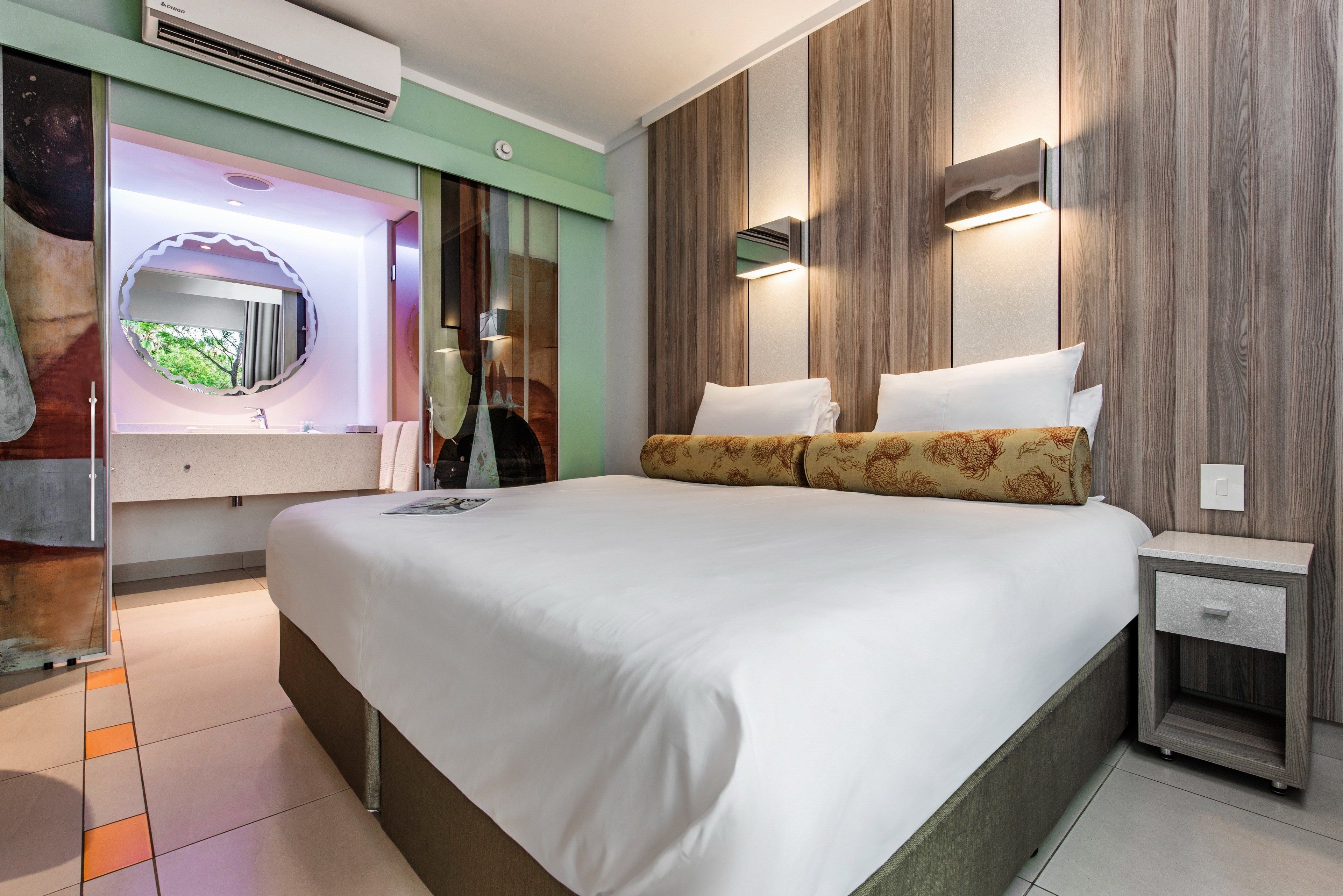 A modern hotel room with a large bed, a vanity with a mirror, and a nightstand.