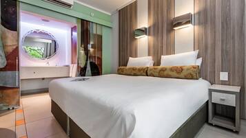 A modern hotel room with a large bed, a vanity with a mirror, and a nightstand.